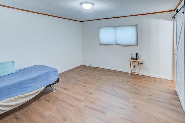 bedroom featuring ornamental molding, a textured ceiling, a barn door, light wood-style floors, and baseboards