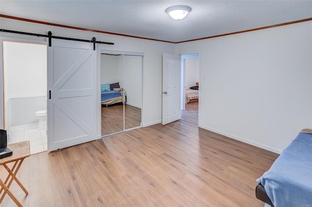 unfurnished bedroom featuring crown molding, light wood-style floors, a closet, a textured ceiling, and a barn door