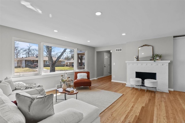 living area with visible vents, baseboards, recessed lighting, light wood-style floors, and a brick fireplace