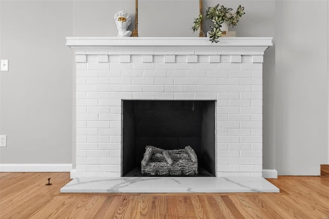 room details with a fireplace with raised hearth, baseboards, and wood finished floors