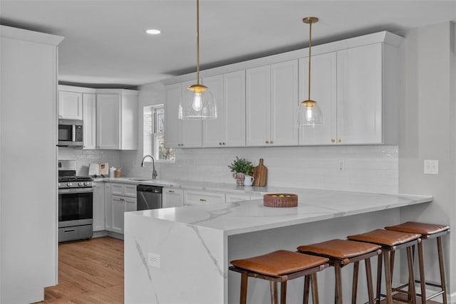 kitchen with a breakfast bar, decorative backsplash, a peninsula, stainless steel appliances, and white cabinetry