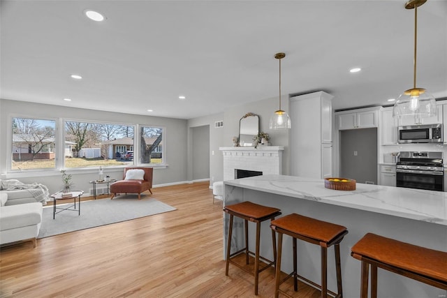 kitchen featuring a kitchen breakfast bar, open floor plan, appliances with stainless steel finishes, light wood finished floors, and light stone countertops