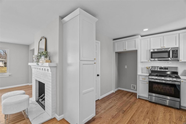 kitchen with appliances with stainless steel finishes, white cabinetry, and light wood-type flooring