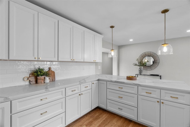 kitchen with a peninsula, white cabinets, light wood-style floors, pendant lighting, and backsplash