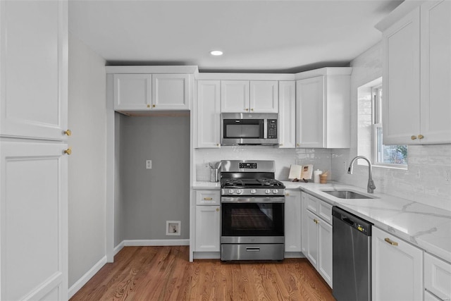 kitchen with a sink, white cabinets, appliances with stainless steel finishes, light wood-type flooring, and backsplash