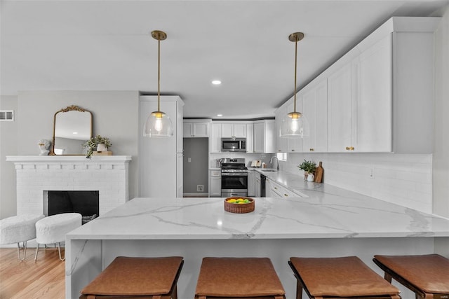 kitchen with light stone counters, white cabinetry, a peninsula, and stainless steel appliances