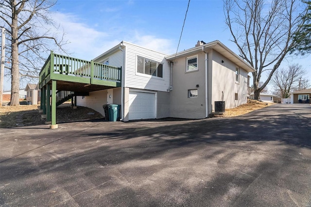 view of property exterior with stucco siding, a deck, central AC, an attached garage, and a carport