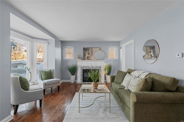 living area with baseboards, a fireplace with raised hearth, and dark wood-style flooring
