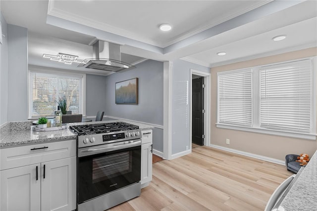 kitchen with crown molding, wall chimney range hood, light wood-type flooring, and stainless steel gas range oven