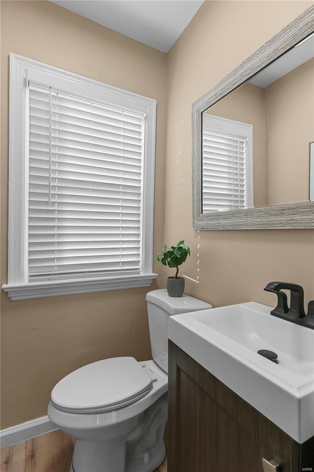 half bath featuring baseboards, toilet, wood finished floors, and vanity