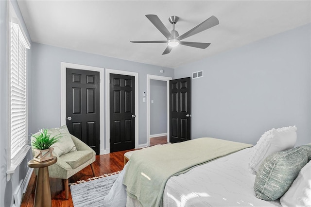 bedroom with ceiling fan, visible vents, baseboards, and wood finished floors