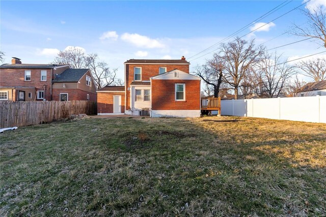 back of property featuring a yard, a chimney, brick siding, and a fenced backyard
