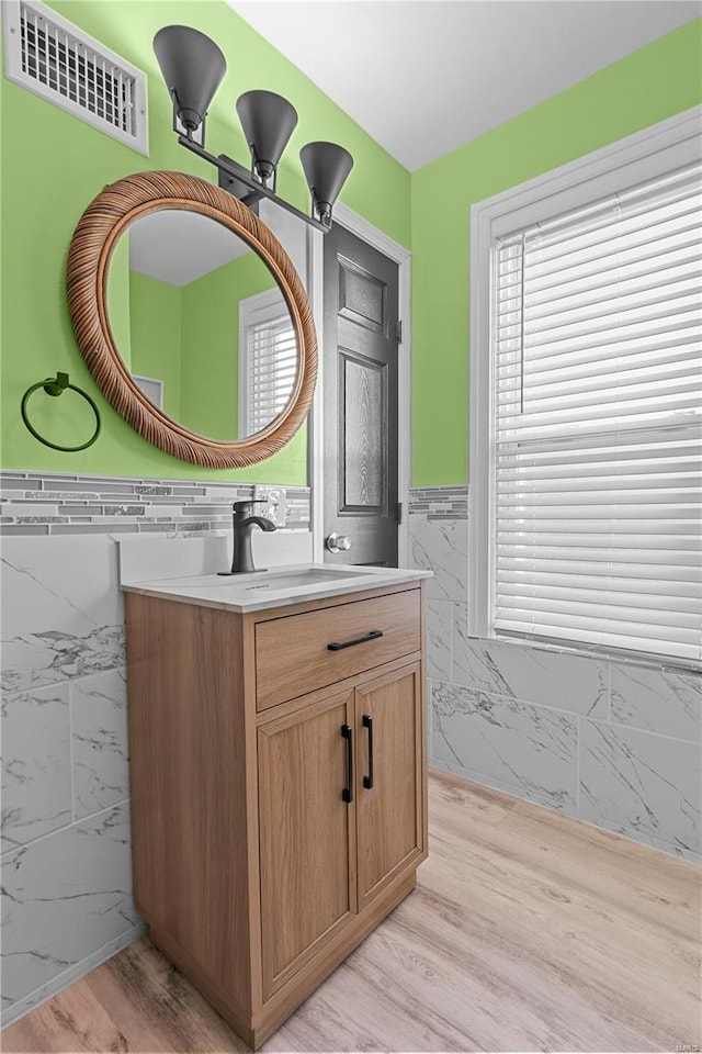 bathroom with visible vents, a wainscoted wall, wood finished floors, tile walls, and vanity
