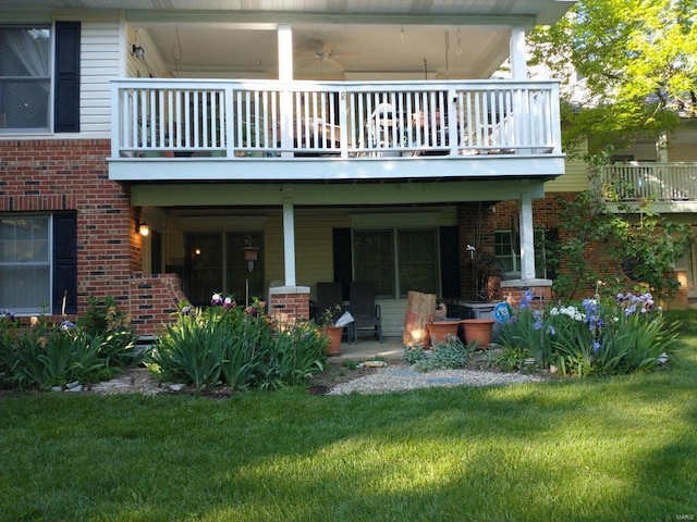 back of house featuring brick siding, a lawn, and a balcony