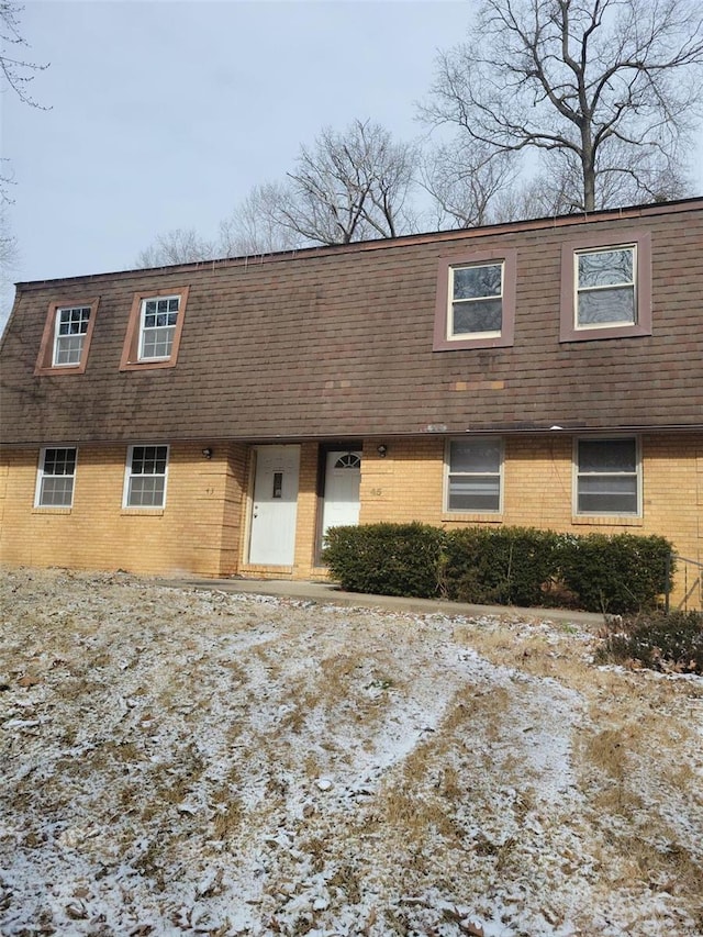 view of front of home featuring mansard roof, brick siding, and a shingled roof