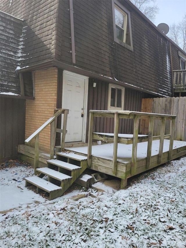 snow covered property entrance with board and batten siding, fence, brick siding, and a wooden deck