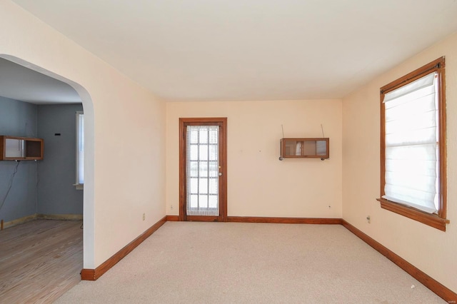 unfurnished room featuring baseboards, arched walkways, and light carpet