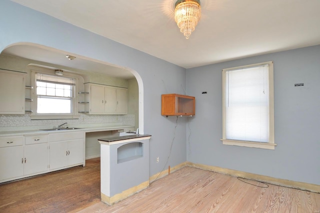 kitchen featuring open shelves, a sink, tasteful backsplash, light wood-style floors, and baseboards