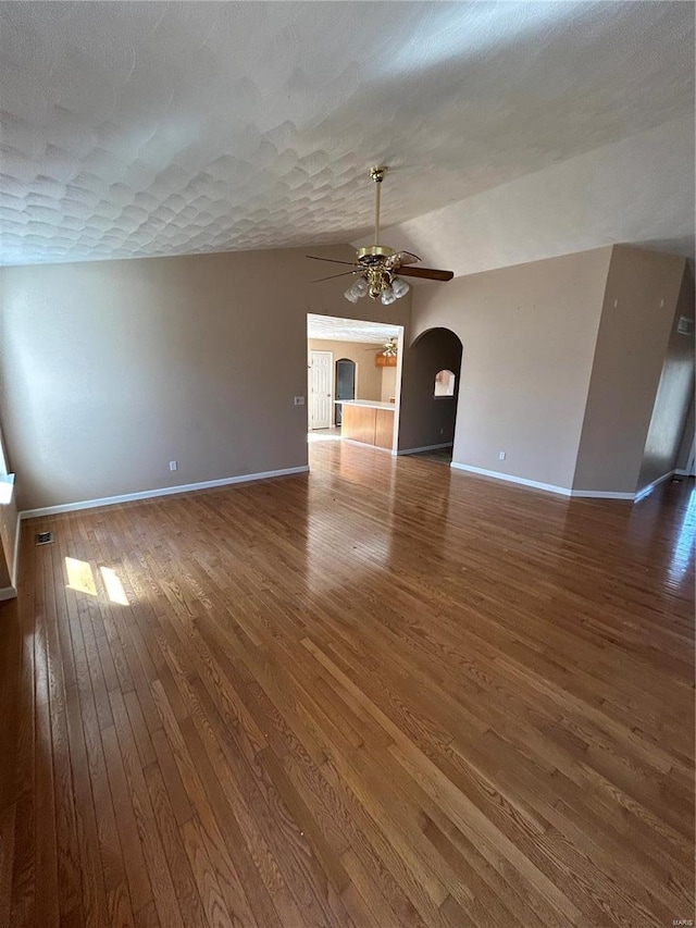 unfurnished living room with baseboards, arched walkways, a textured ceiling, a ceiling fan, and wood-type flooring