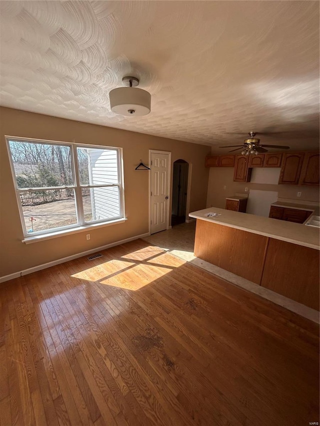 interior space with light wood-type flooring, visible vents, a ceiling fan, arched walkways, and baseboards