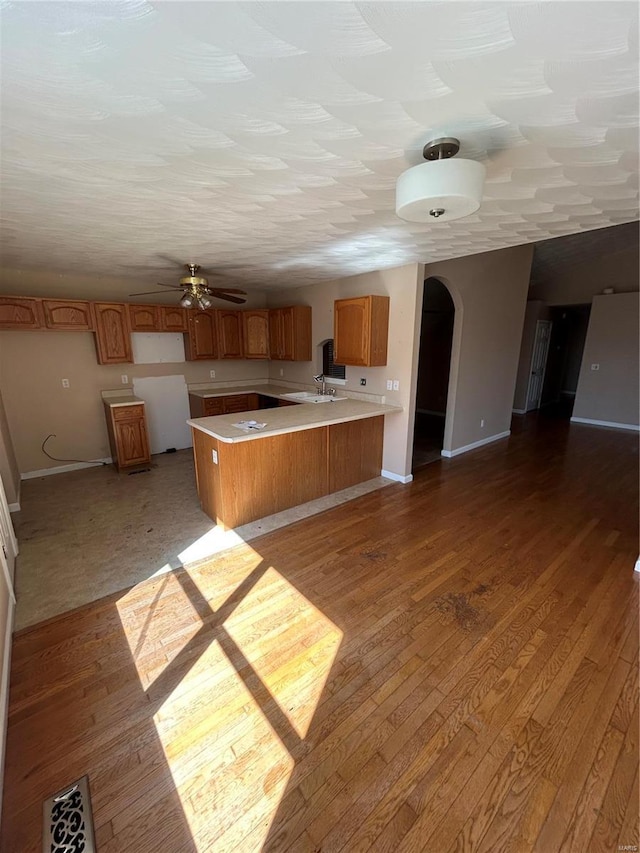 kitchen with brown cabinets, light wood-style flooring, a sink, arched walkways, and a peninsula