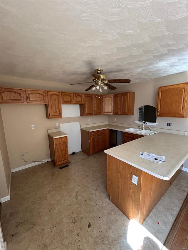 kitchen featuring brown cabinets, a sink, a peninsula, baseboards, and ceiling fan