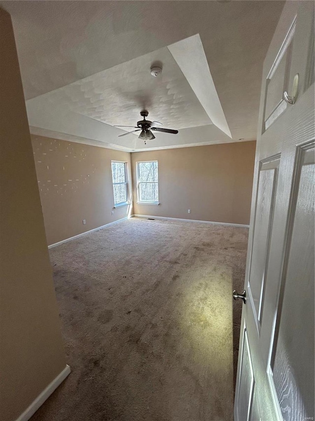 spare room with ceiling fan, baseboards, a raised ceiling, and carpet