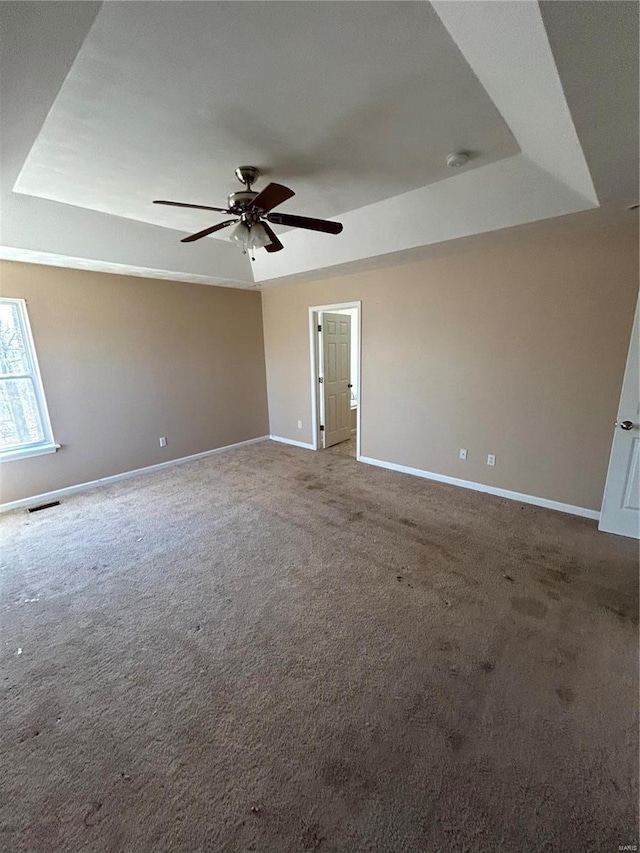 carpeted spare room with a tray ceiling, baseboards, visible vents, and ceiling fan