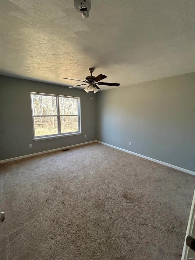 carpeted spare room with visible vents, baseboards, and ceiling fan