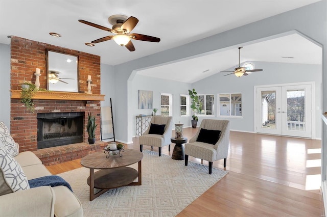 living area with a fireplace, lofted ceiling, wood finished floors, and french doors