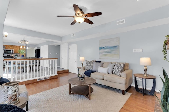 living area featuring visible vents, ceiling fan with notable chandelier, baseboards, and light wood-style floors