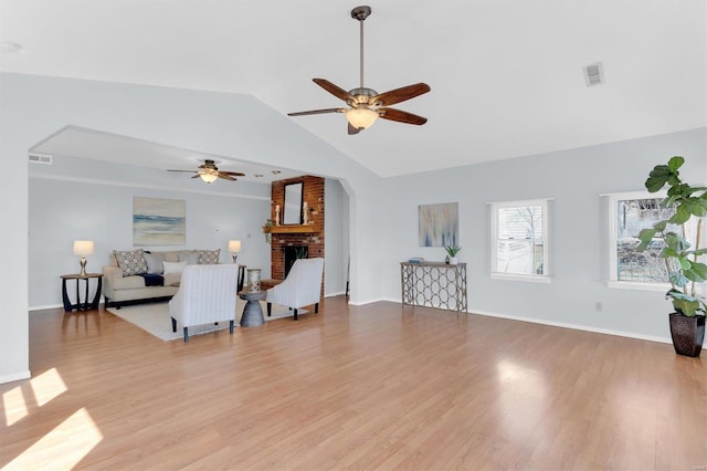 living room with visible vents, light wood-style flooring, a brick fireplace, ceiling fan, and vaulted ceiling