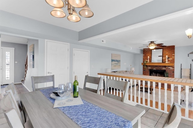 dining area with visible vents, a brick fireplace, baseboards, stairway, and ceiling fan with notable chandelier