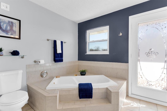 full bath with tile patterned floors, a garden tub, toilet, and a textured ceiling