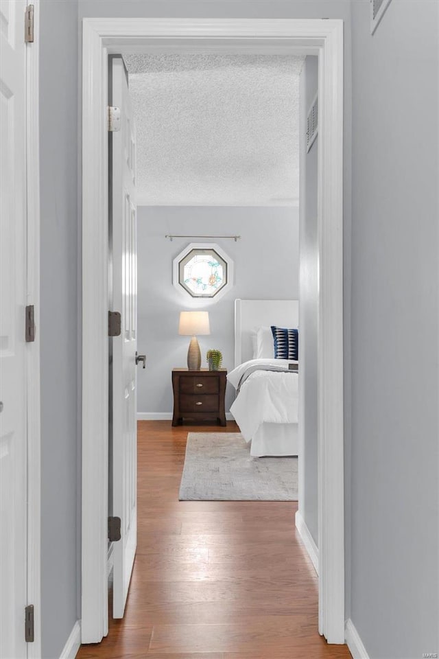 bedroom featuring baseboards, a textured ceiling, and wood finished floors