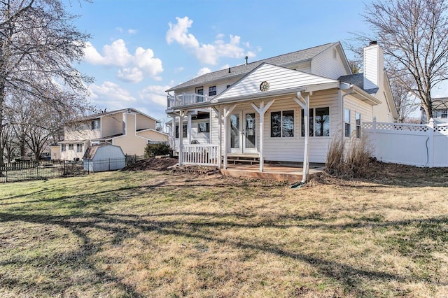 back of house with fence, covered porch, a lawn, a chimney, and a balcony