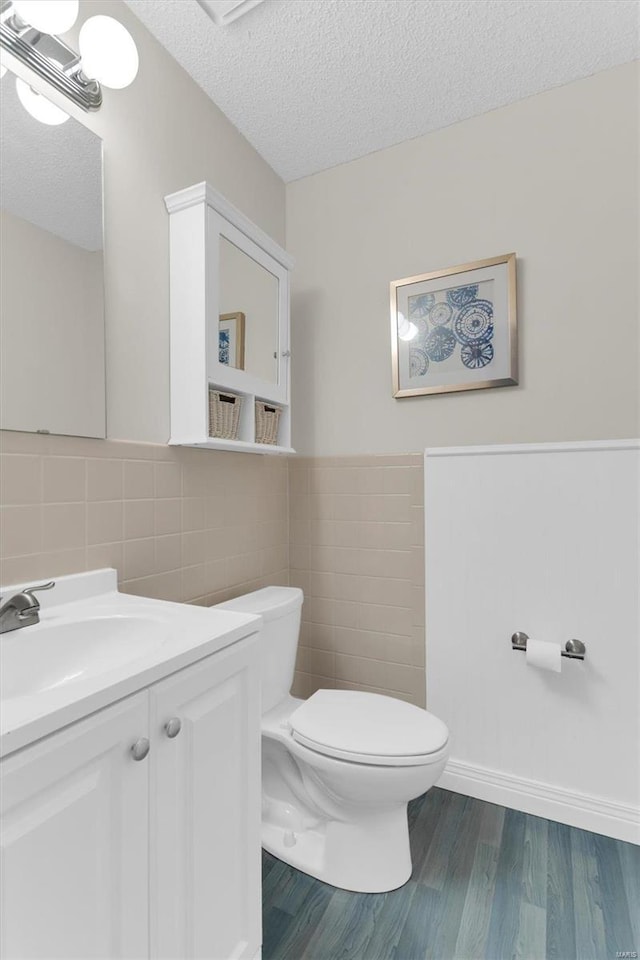 half bathroom featuring toilet, a textured ceiling, wood finished floors, tile walls, and vanity