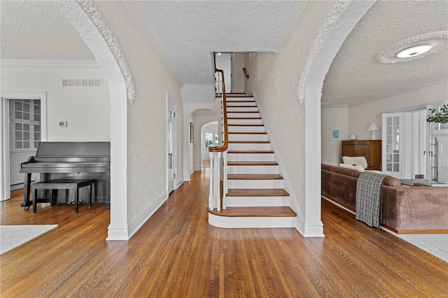 stairway featuring wood finished floors, visible vents, arched walkways, crown molding, and a textured wall