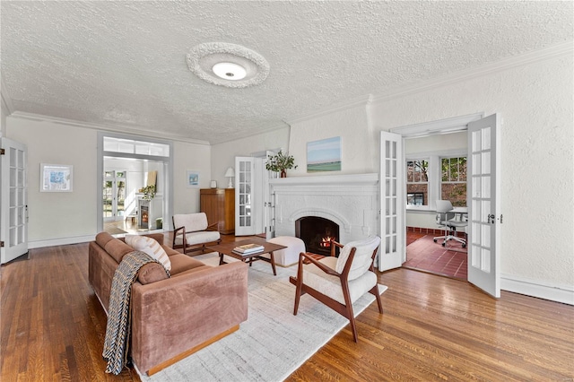 living area with wood finished floors, ornamental molding, a warm lit fireplace, french doors, and a textured wall