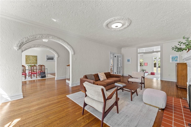 living room featuring crown molding, a textured wall, wood finished floors, arched walkways, and a textured ceiling