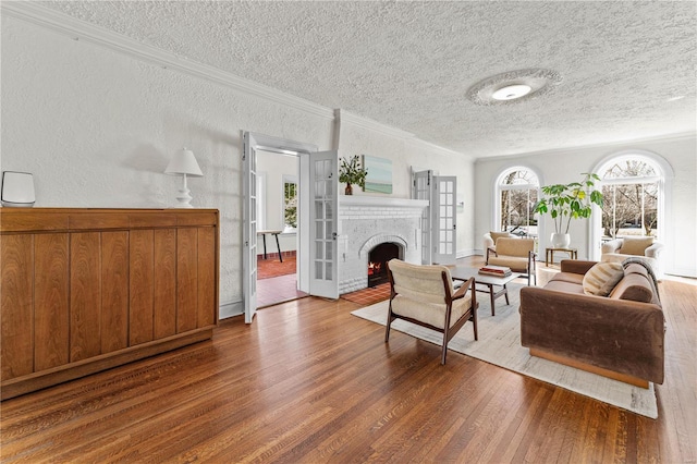 living room featuring wood finished floors, ornamental molding, a textured ceiling, a brick fireplace, and a textured wall