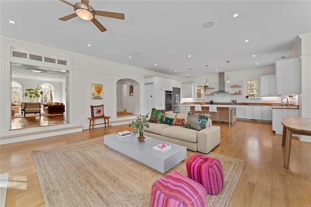 living room featuring crown molding, ceiling fan, recessed lighting, light wood-style flooring, and arched walkways