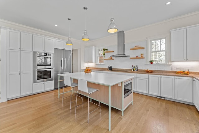 kitchen featuring a kitchen breakfast bar, wall chimney range hood, appliances with stainless steel finishes, and ornamental molding