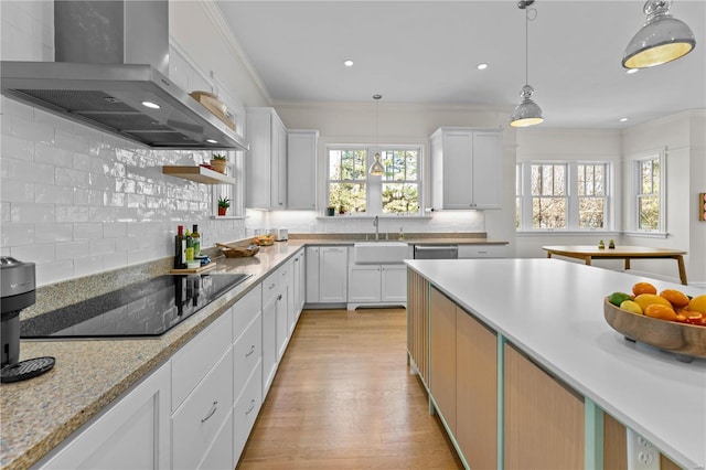 kitchen with black electric stovetop, backsplash, wall chimney exhaust hood, and crown molding