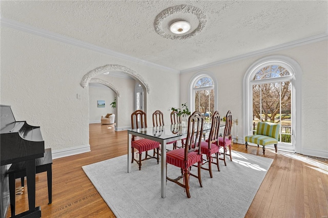 dining area with a textured ceiling, wood finished floors, a textured wall, and ornamental molding