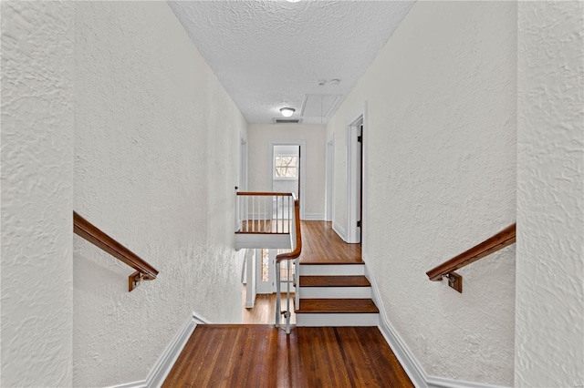 stairs with wood finished floors, baseboards, visible vents, a textured ceiling, and a textured wall