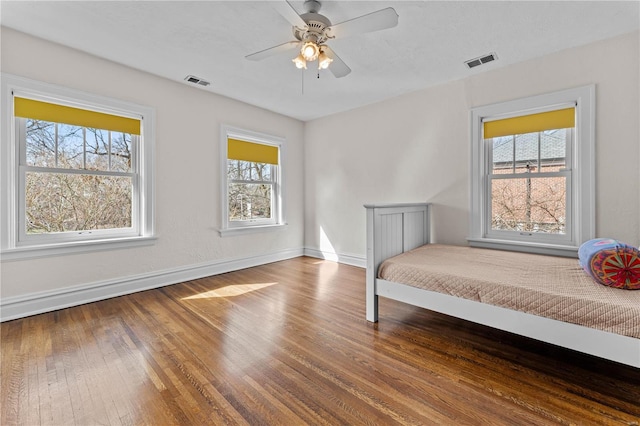 bedroom with ceiling fan, visible vents, baseboards, and hardwood / wood-style floors