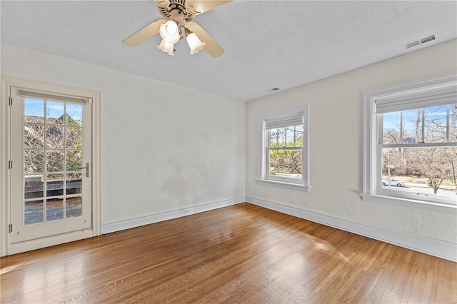 spare room with a ceiling fan, visible vents, wood finished floors, baseboards, and a textured ceiling