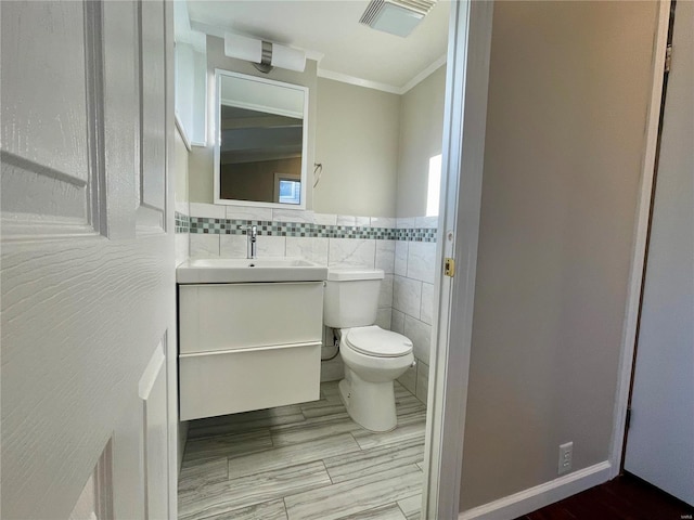 bathroom with visible vents, crown molding, toilet, vanity, and tile walls