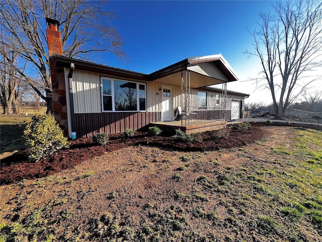 view of front of house featuring board and batten siding, a porch, a garage, and a chimney